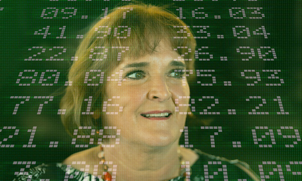 La Dra. Betty Simkins sonríe para una foto con los números del mercado de valores superpuestos al fondo.