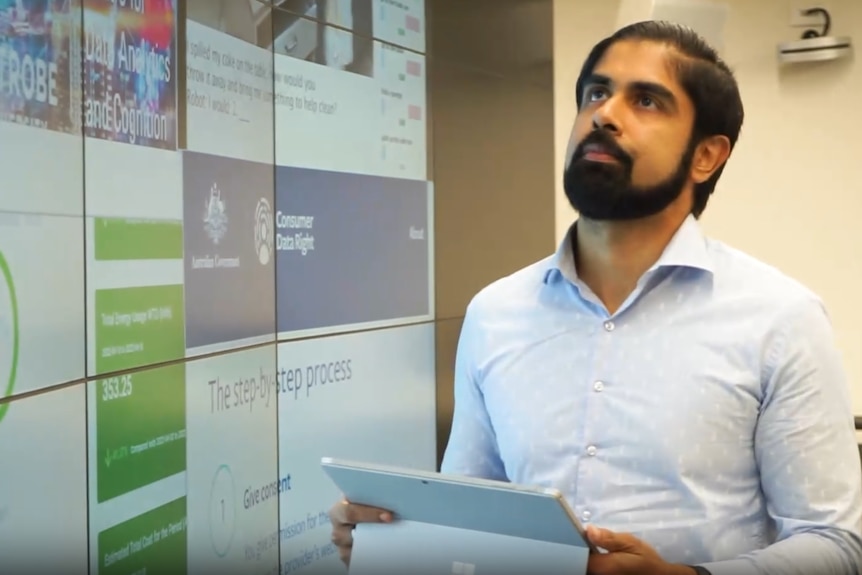 Un hombre con una camisa azul botón y una barda sosteniendo una tableta.